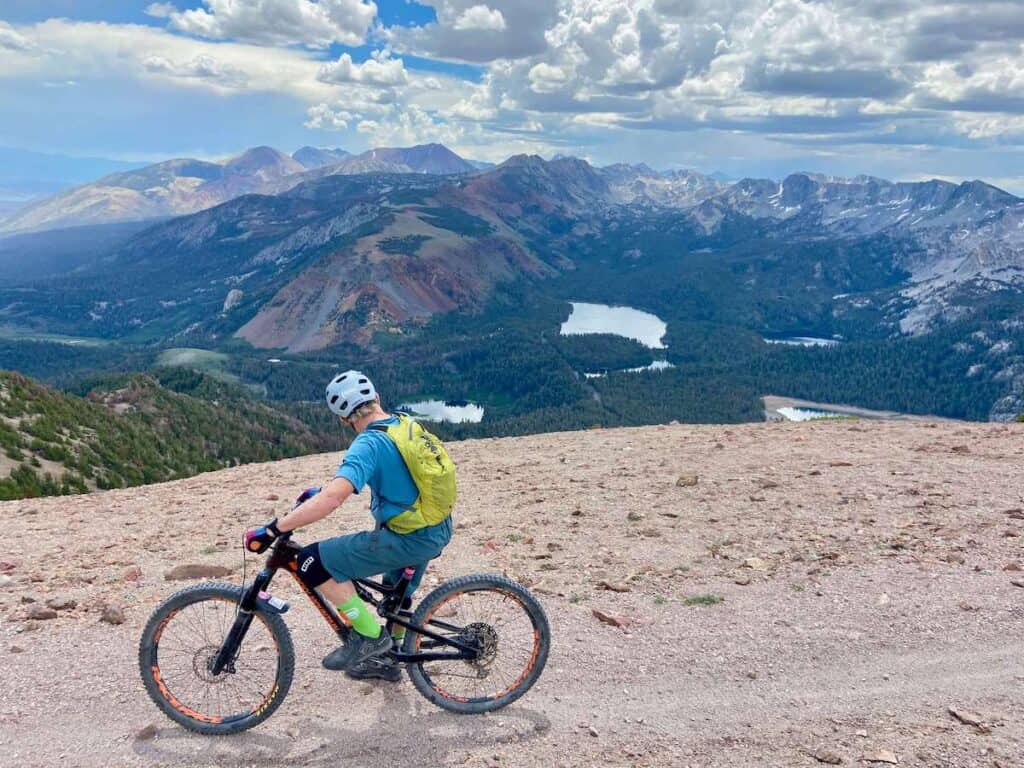 Mountain biker stopped on trail at the top of Mammoth Bike Park looking out over stunning mountain and lake view